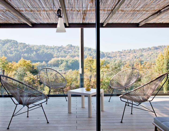 Terrasse en bois d'accoya intérieure de couleur claire. 2 chaises en osiers avec au milieu une petite table blanche. Pergola en bambou. Arrière plan, vision sur la forêt