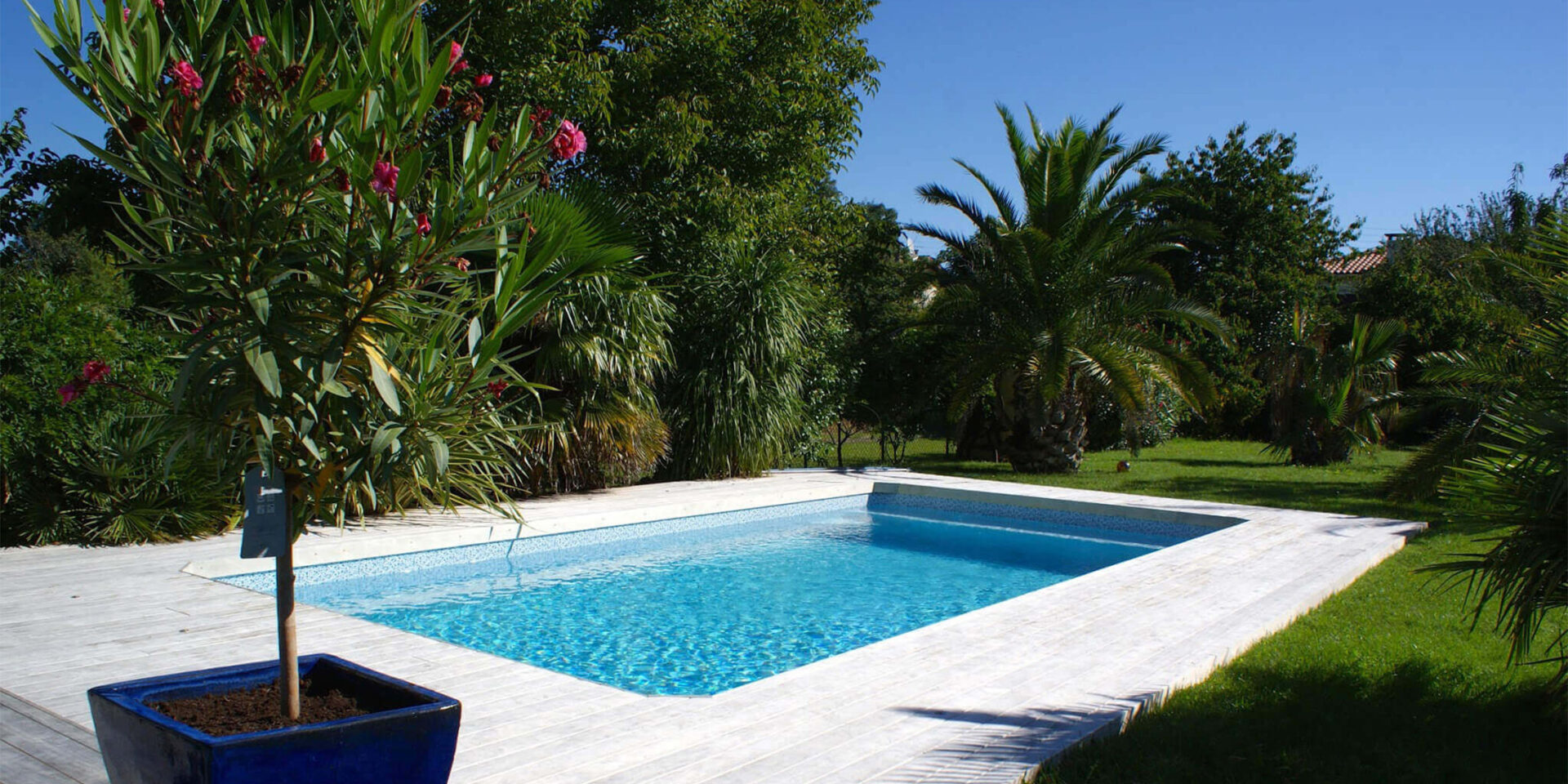 Dans le jardin vert, une piscine bleue est entourée d'une terrasse en accoya grise claire. 