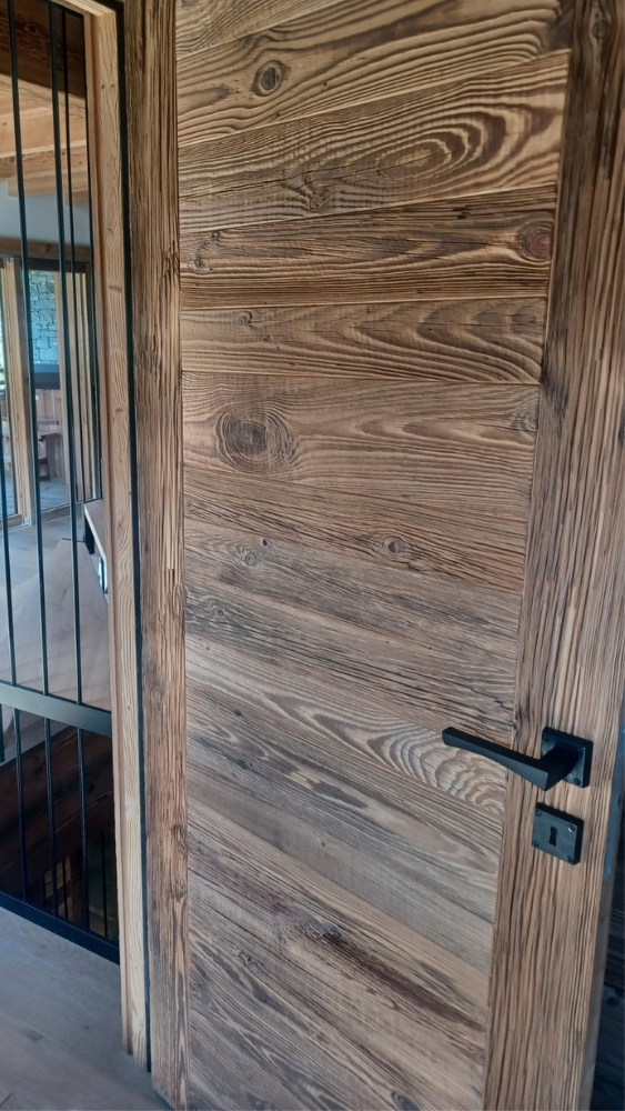 Porte en vieux bois aux nuances marron, installée en intérieur avec les menuiseries noir mat.