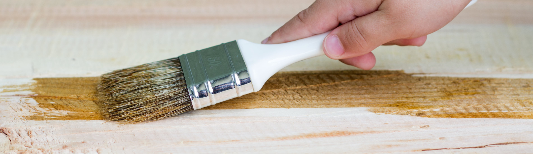 Le parquet est de couleur clair. Une main d'enfant tient un pinceau et applique une couche de finition. 