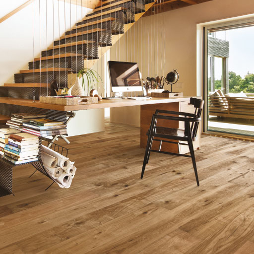 Photo d'ambiance avec un parquet et un escalier en bois, un bureau, une chaise. Une baie vitrée donne sur le jardin.