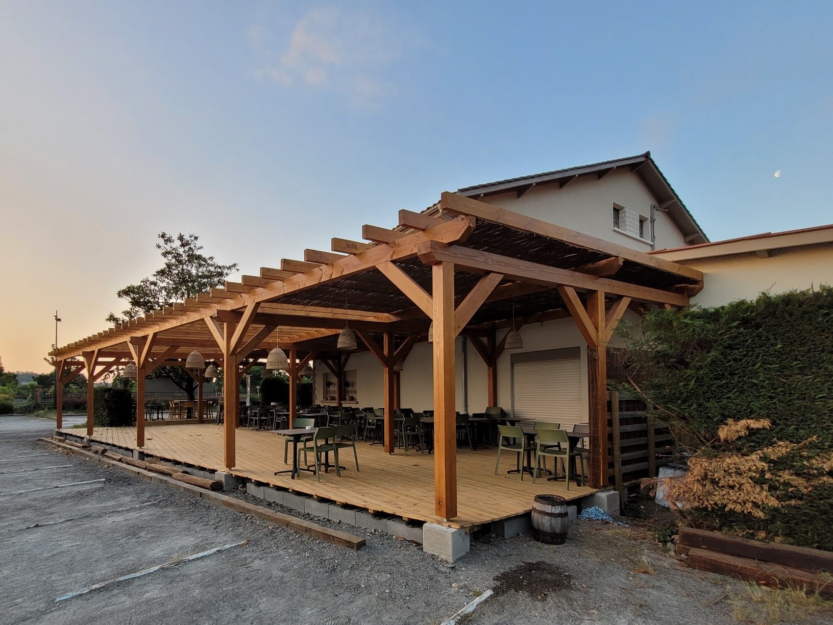 Chantier client. Terrasse d'un restaurant avec installation d'une pergola en douglas et de couleur claire. Le ciel est bleu et le soleil se couche.