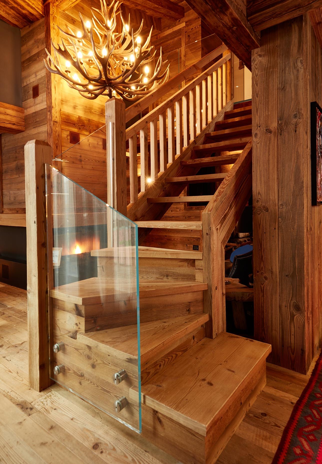 Grand escalier en bois avec le sol en vieux bois. Un magnifique lustre orne le plafond.