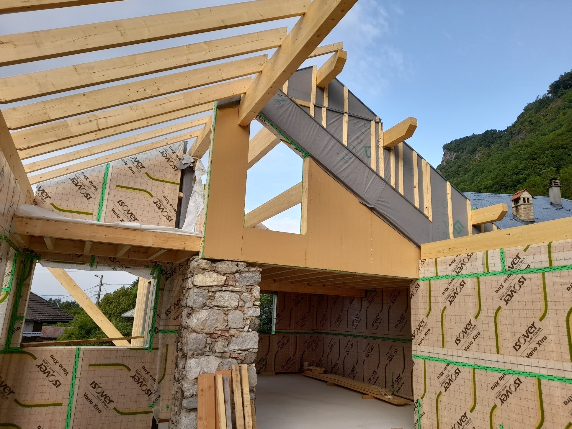 Photo prise à l'étage de la maison en rénovation. La moitiée de la l'ossature bois est installée. La structure est de couleur clair, les dalles au sol sont installées.