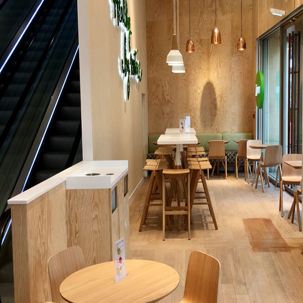 Petite salle de restaurant réalisée en panneaux contreplaqués CTBX tout okoumé. Il y a des tables, des chaises de couleur clairs. Des spots de lumières sont accrochés au plafond. 